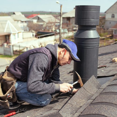 a professional master (roofer) with hammer repairs the roof. Repair Asphalt Shingles or Bitumen Tiles on the Rooftop Outdoor